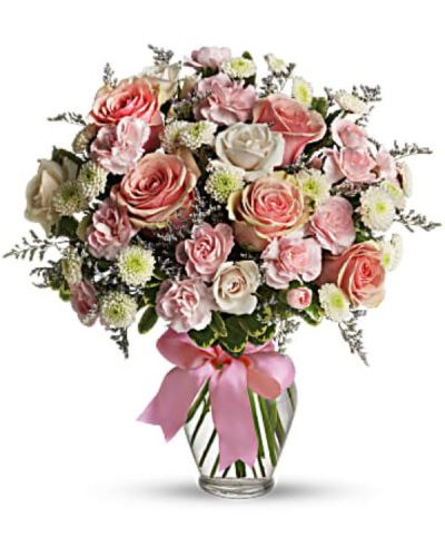 Pretty pink roses, spray roses and miniature carnations, white button spray chrysanthemums, lavender limonium and green pittosporum fill a spring glass vase that's wrapped with a pink satin ribbon. It's confection perfection!