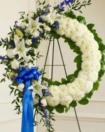 <p>With blue flowers that symbolize truth and white blooms that signify honor, this standing wreath arrangement beautifully reflects the love and sympathy that is in your heart. Exquisitely crafted by our expert florists, it features a gathering of fresh blue delphinium, white roses, lilies, mums, carnations, monte casino and more accented by variegated pittosporum, ruscus and salal. Appropriate for family, friends and business associates to send directly to the funeral home.</p>